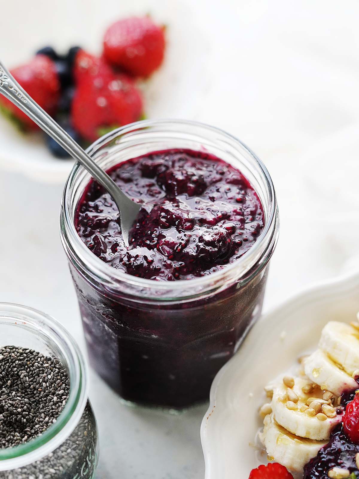 A jar with berry chia jam and a spoon.