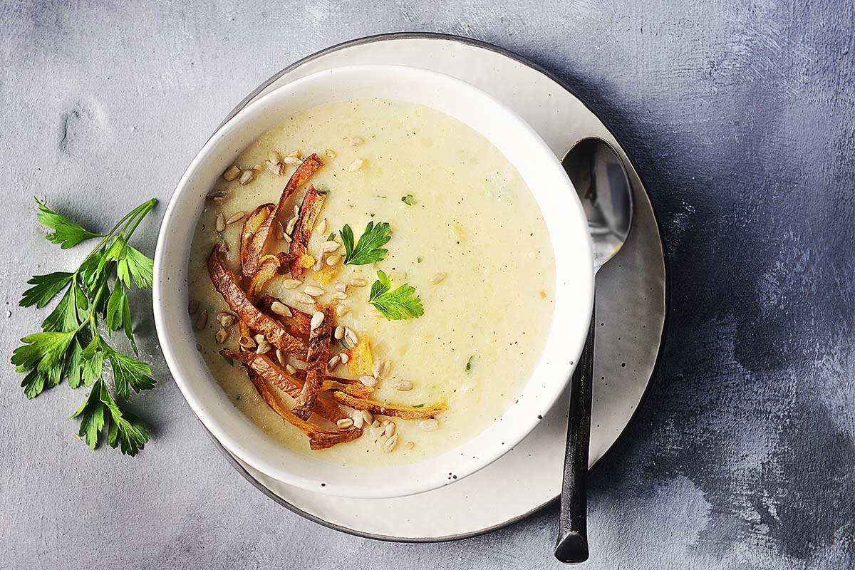 A bowl with creamy potato soup garnished with parsley and seeds.