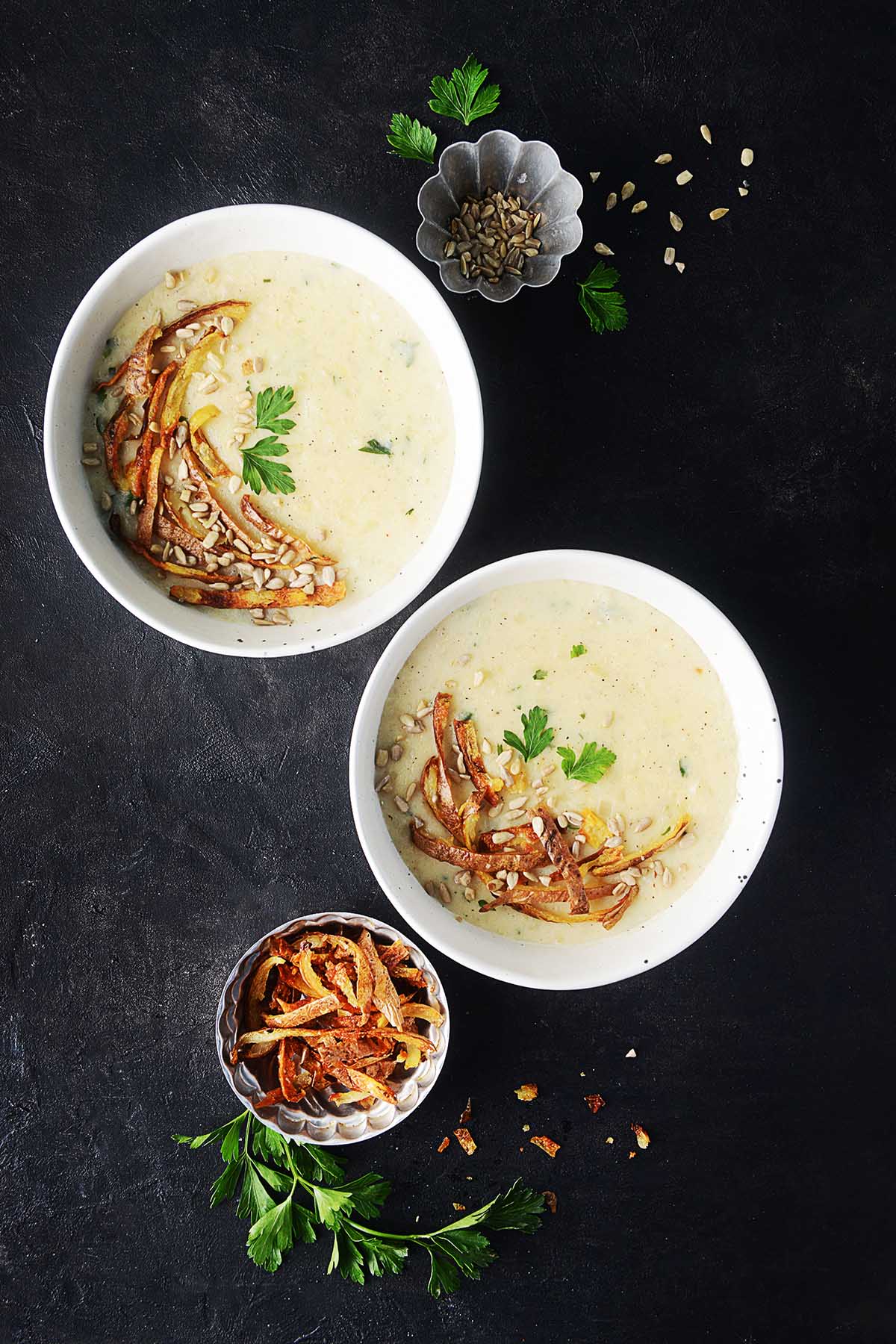 Two bowls of dairy free potato soup garnished with parsley and seeds.