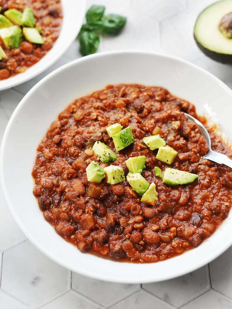 Vegetarian tofu bean chili in a white bowl topped with cubed avocado.