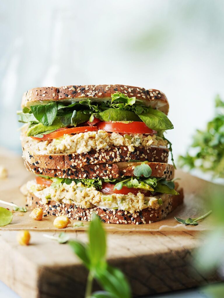 A stacked Vegan Chickpea Salad Sandwich on a cutting board.