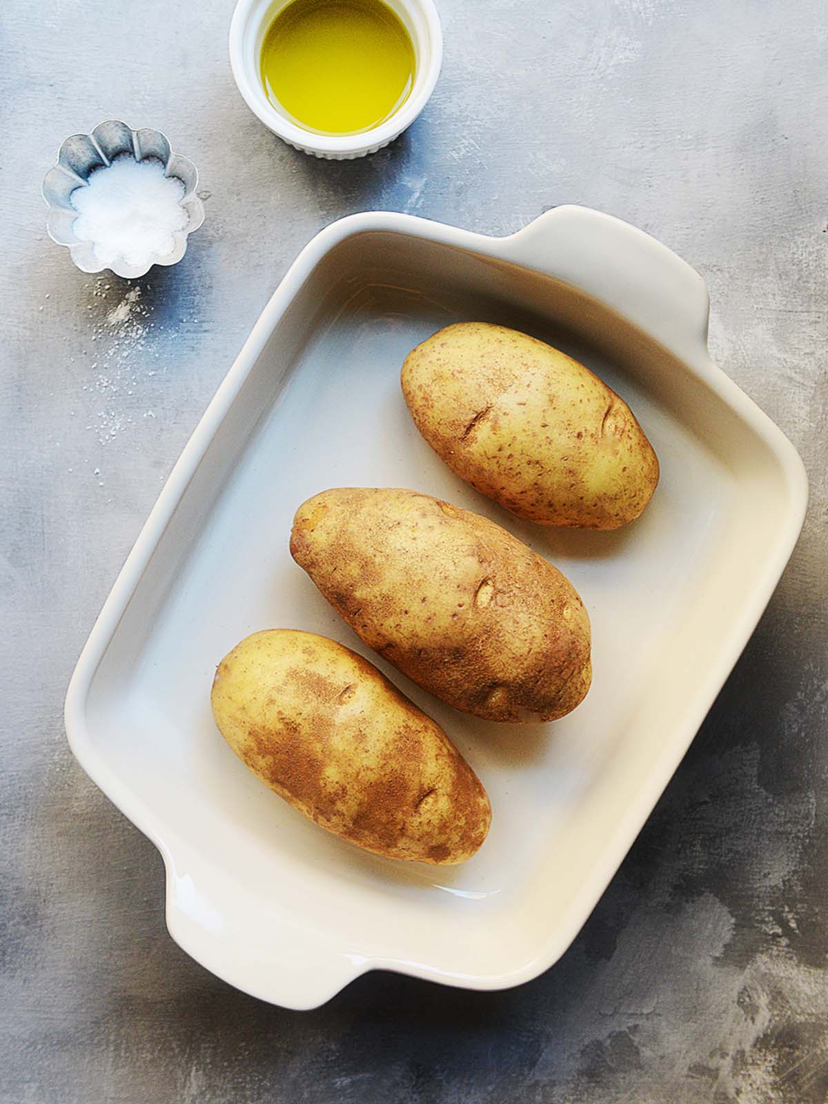 Three large russet potatoes placed in a baking tray.