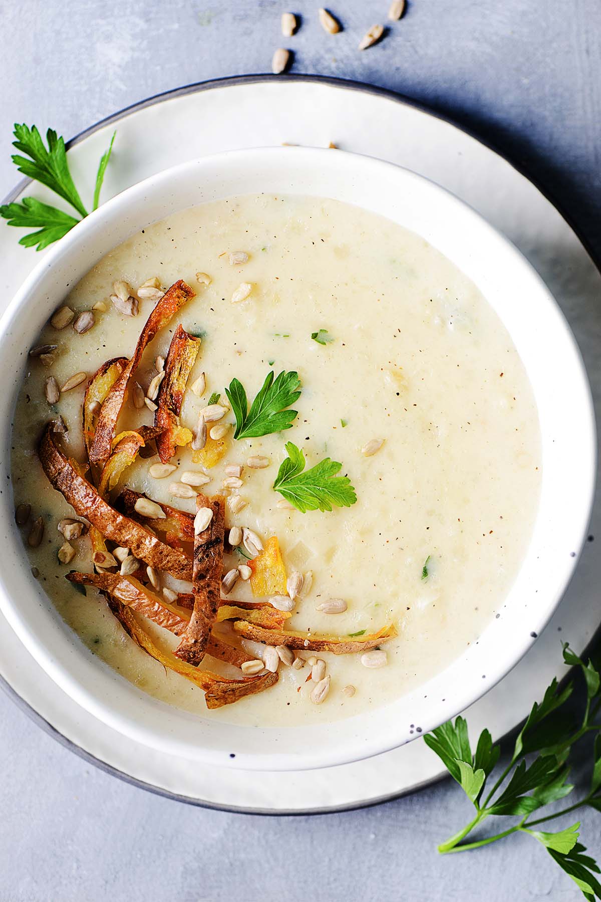 A bowl with creamy potato soup garnished with parsley and seeds.