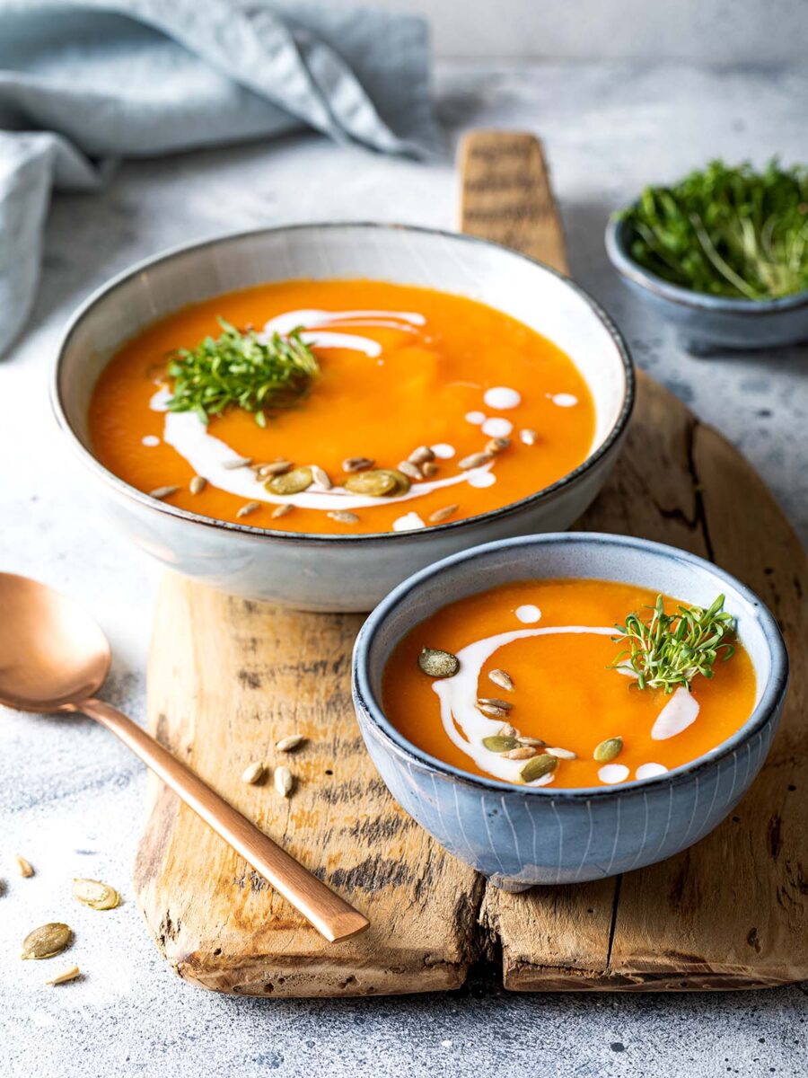 Two bowls of Pumpkin Sweet Potato Soup on a piece of wood.