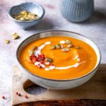 A bowl of creamy orange soup on a piece of wood.