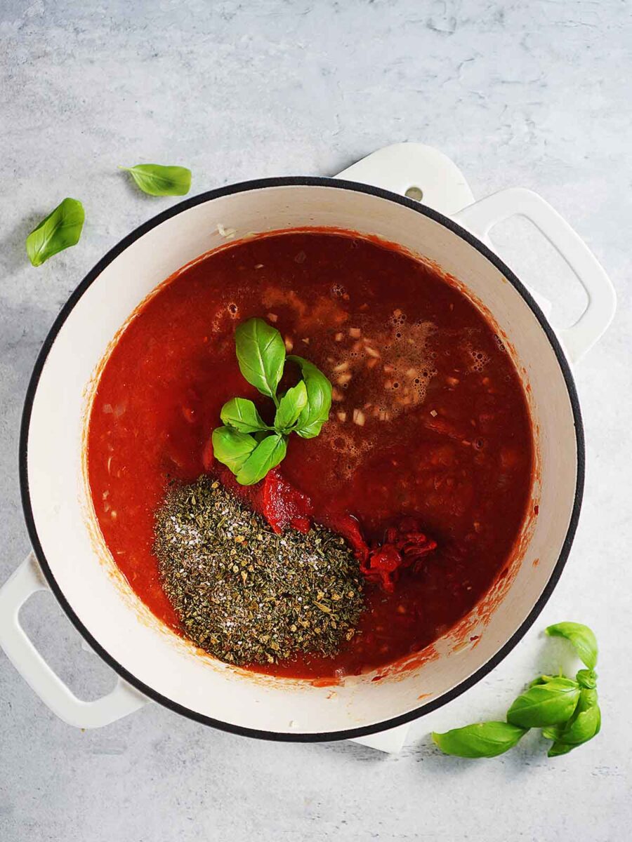 A saucepan with tomato sauce and herbs and a basil sprig.