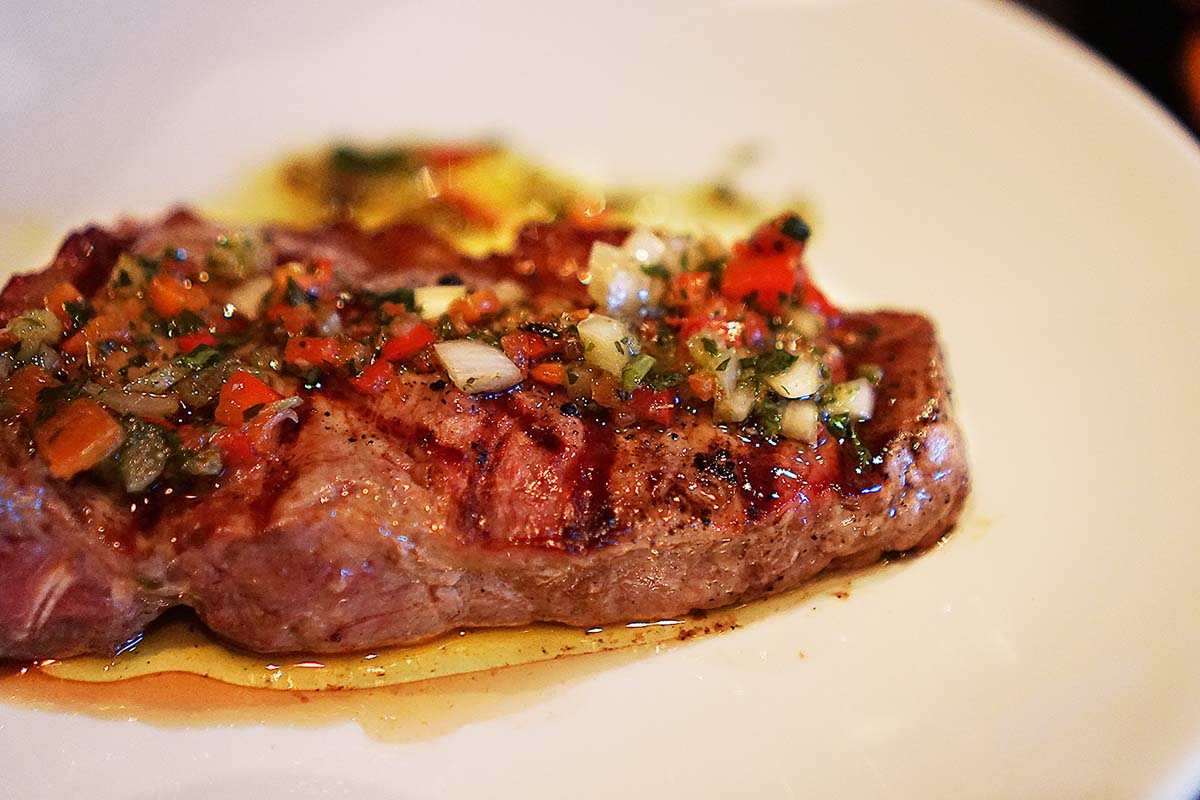 A steak with chimichurri on a white plate.