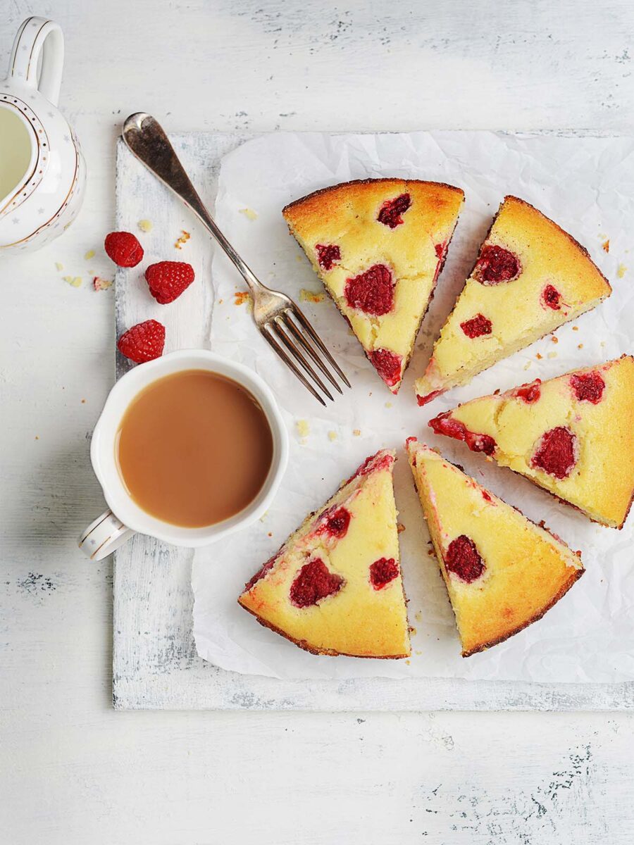 A raspberry cake sliced into triangles with a coffee cup on the side.