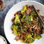 A white plate with beef and broccoli with chopsticks on the side.