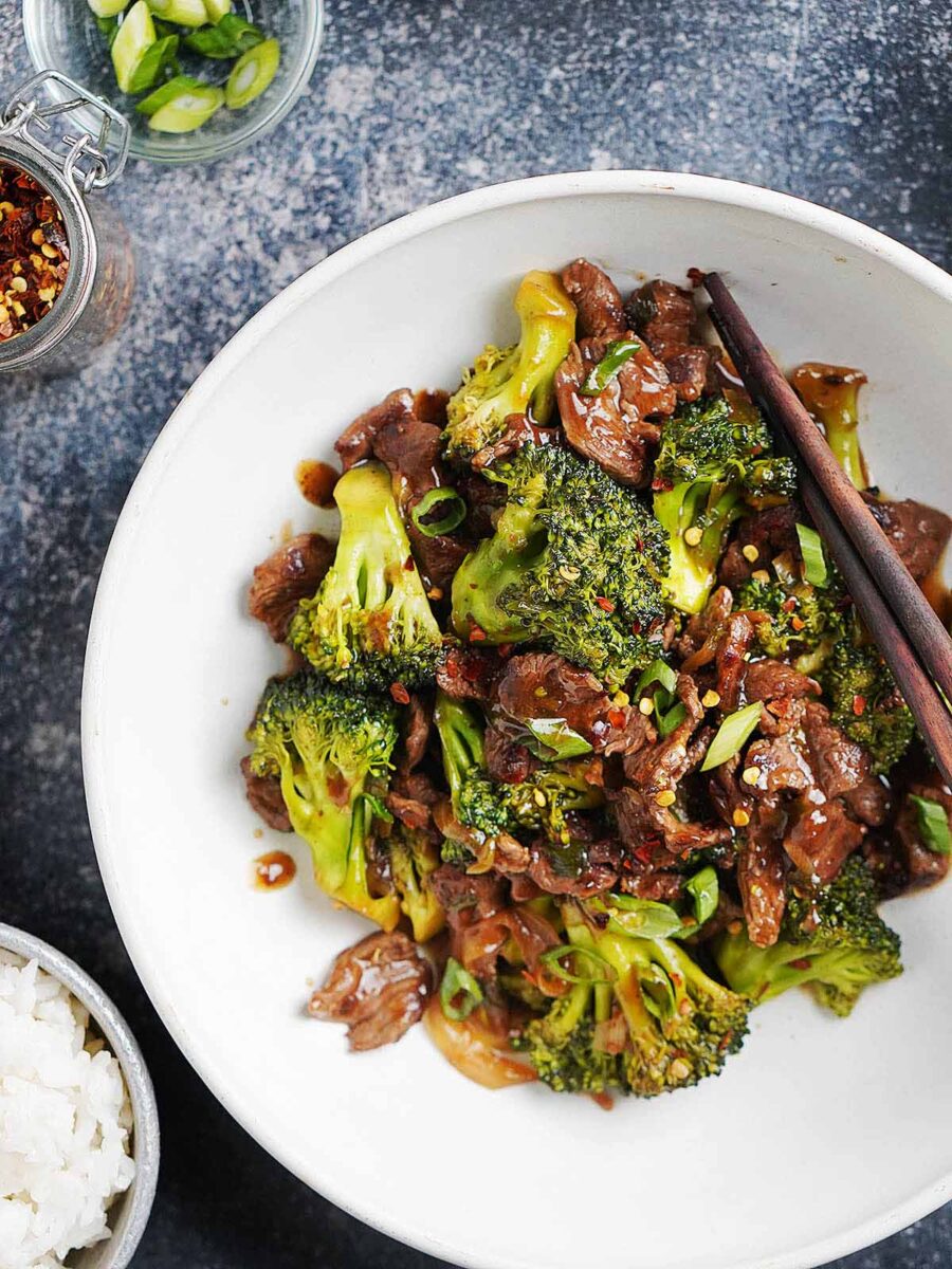 A white plate with beef and broccoli with chopsticks on the side.