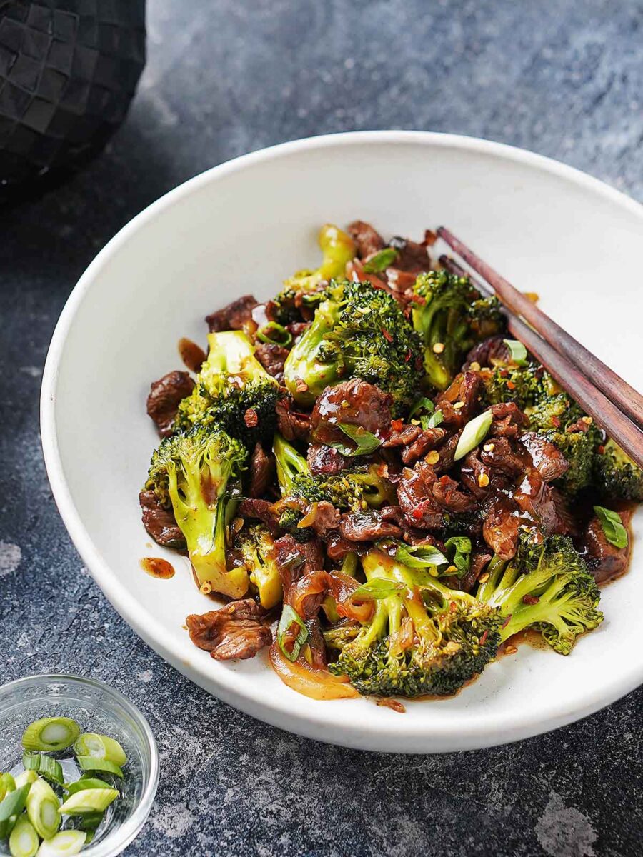 A white plate with beef and broccoli with chopsticks on the side.