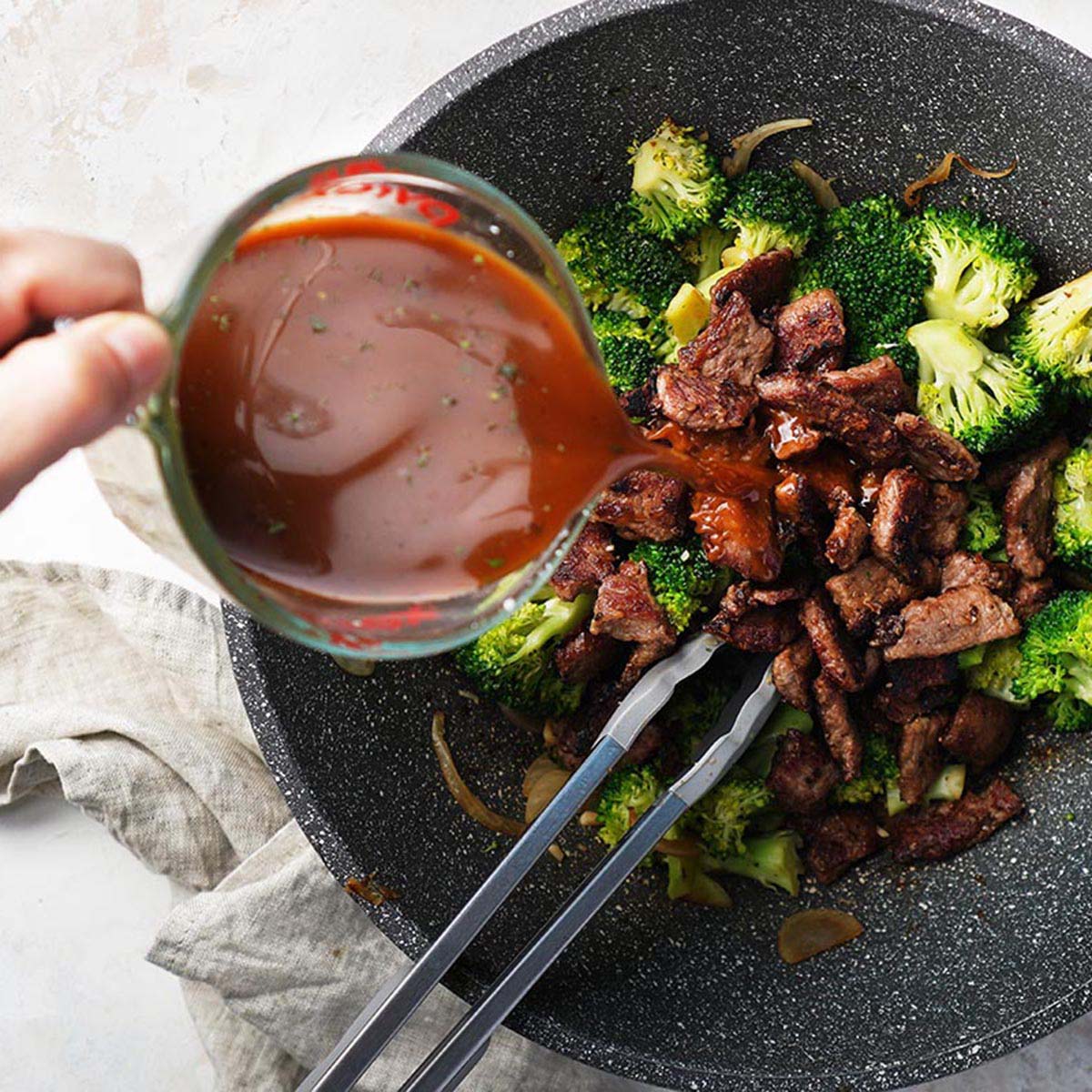 Adding asian sauce on cooked broccoli, onions and garlic on a wok.
