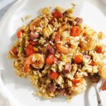 A white place with cajun shrimp and rice with a fork on a metal counter.