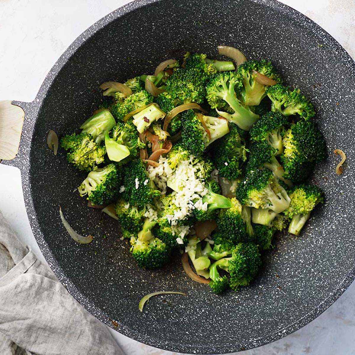 Cooking broccoli, onions and garlic on a wok.