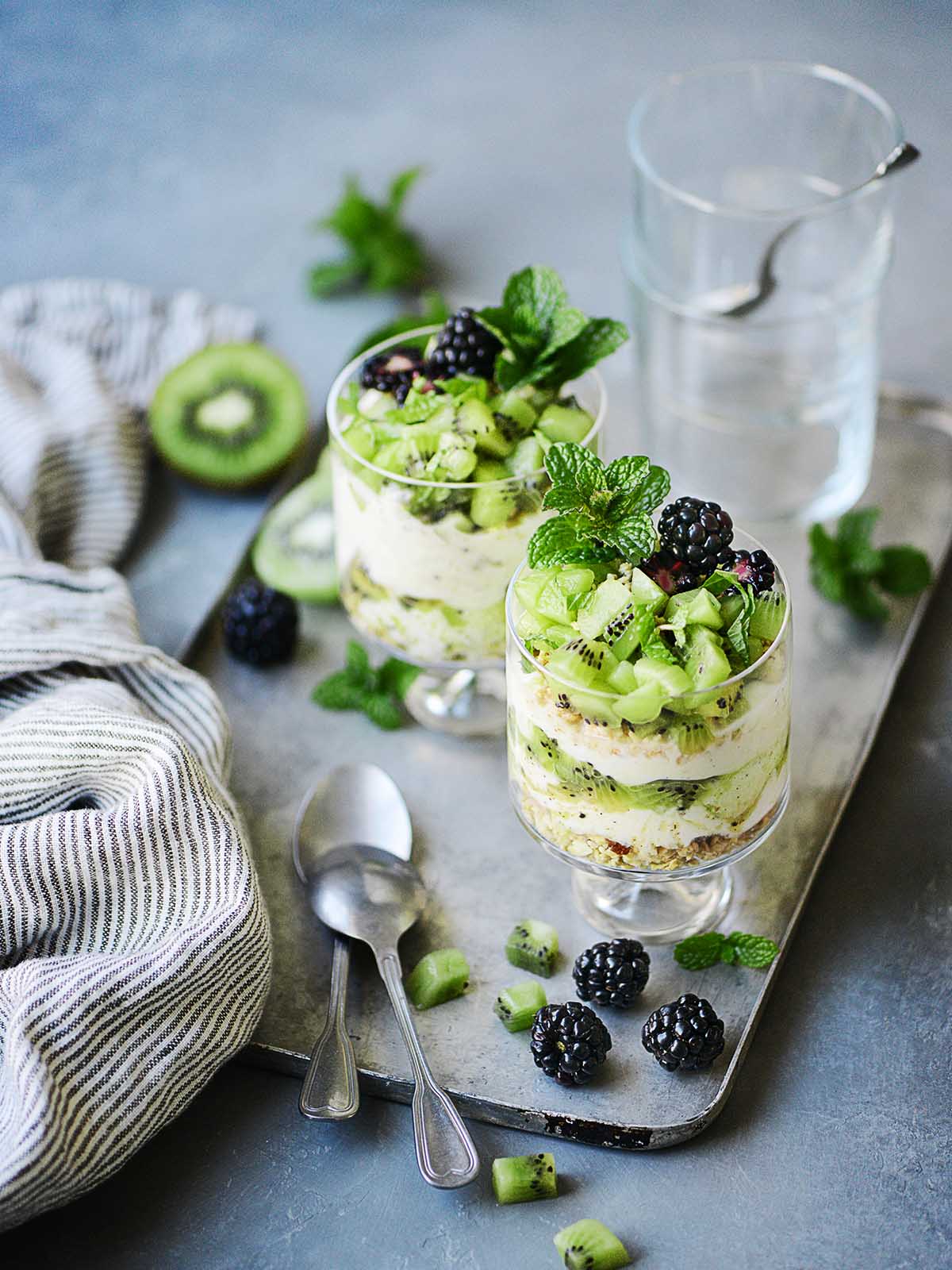 Two cute glasses with parfait placed on a metal tray.