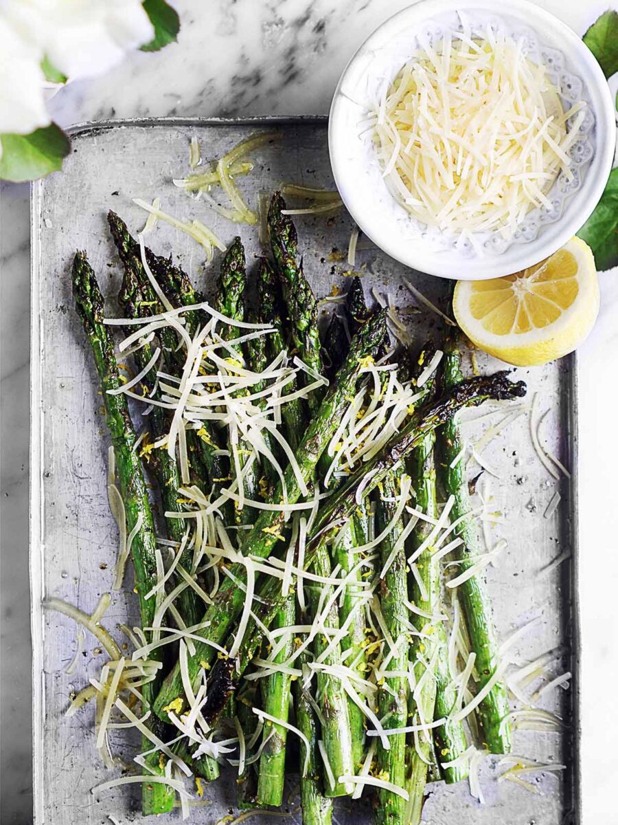 Asparagus on a tray topped with lemon zest and shredded parmesan.