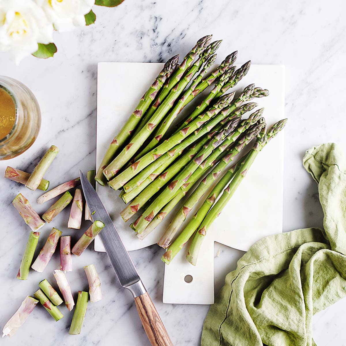A bunch of asparagus on a cutting board with a knife on the side.