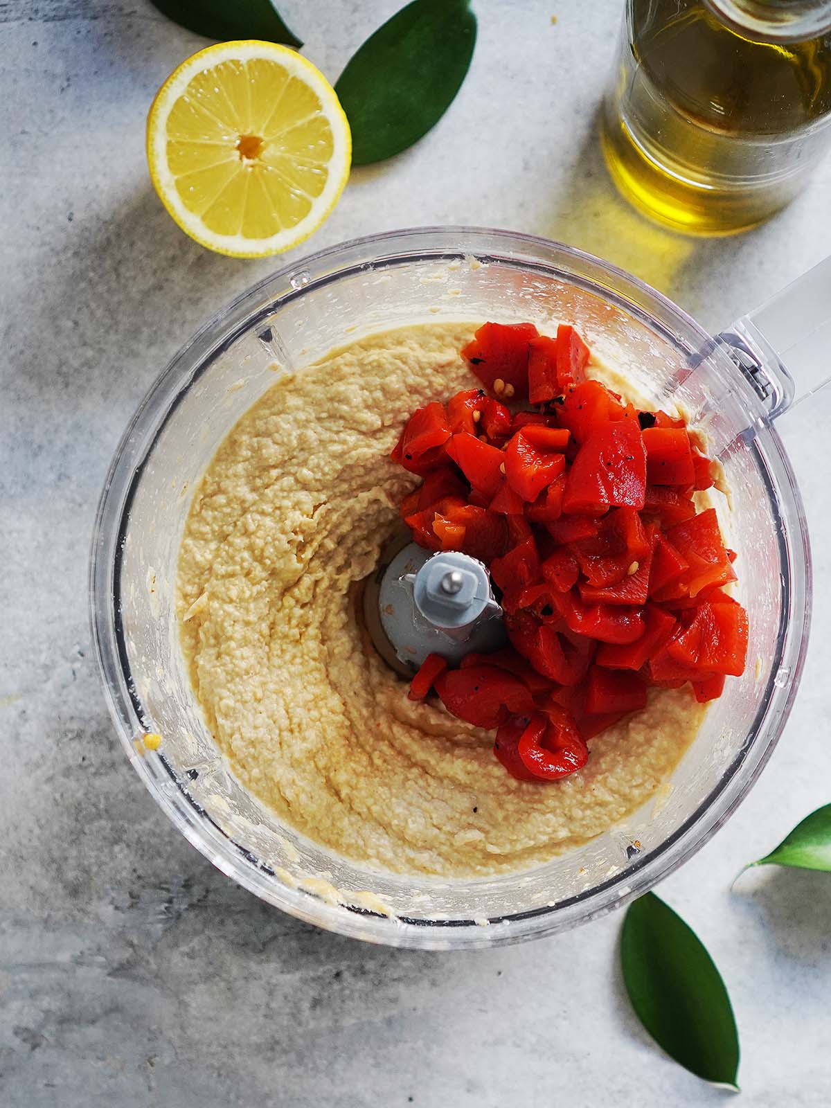 Food processor container with tahini and chopped garlic and the addition of roasted peppers.