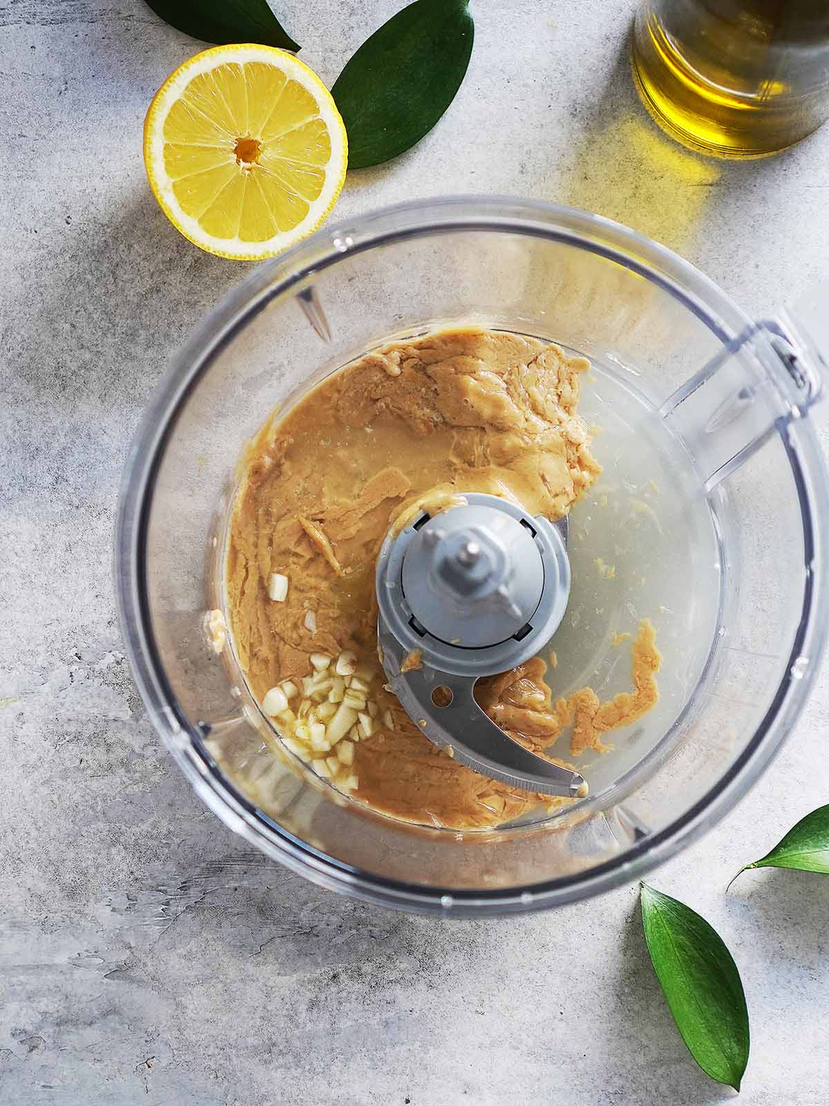 Food processor container with tahini and chopped garlic.