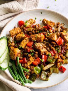 Kung pao pork on a plate garnished with cucumbers and green beans on the side.