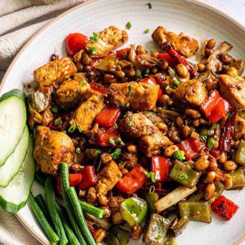 Kung pao pork on a plate garnished with cucumbers and green beans on the side.