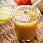 The vinaigrette is inside a glass container and has a whisk on top.