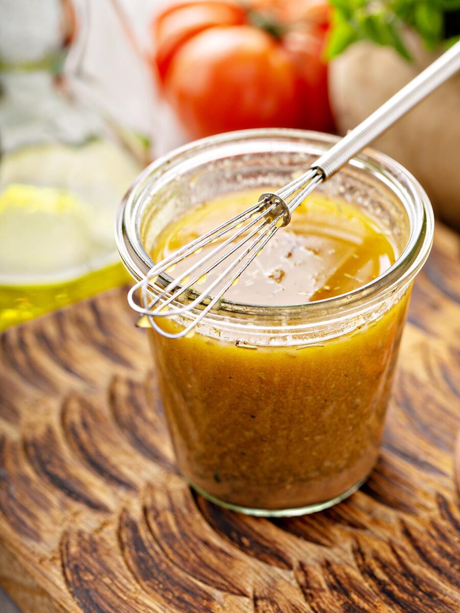 The vinaigrette is inside a glass container and has a whisk on top.