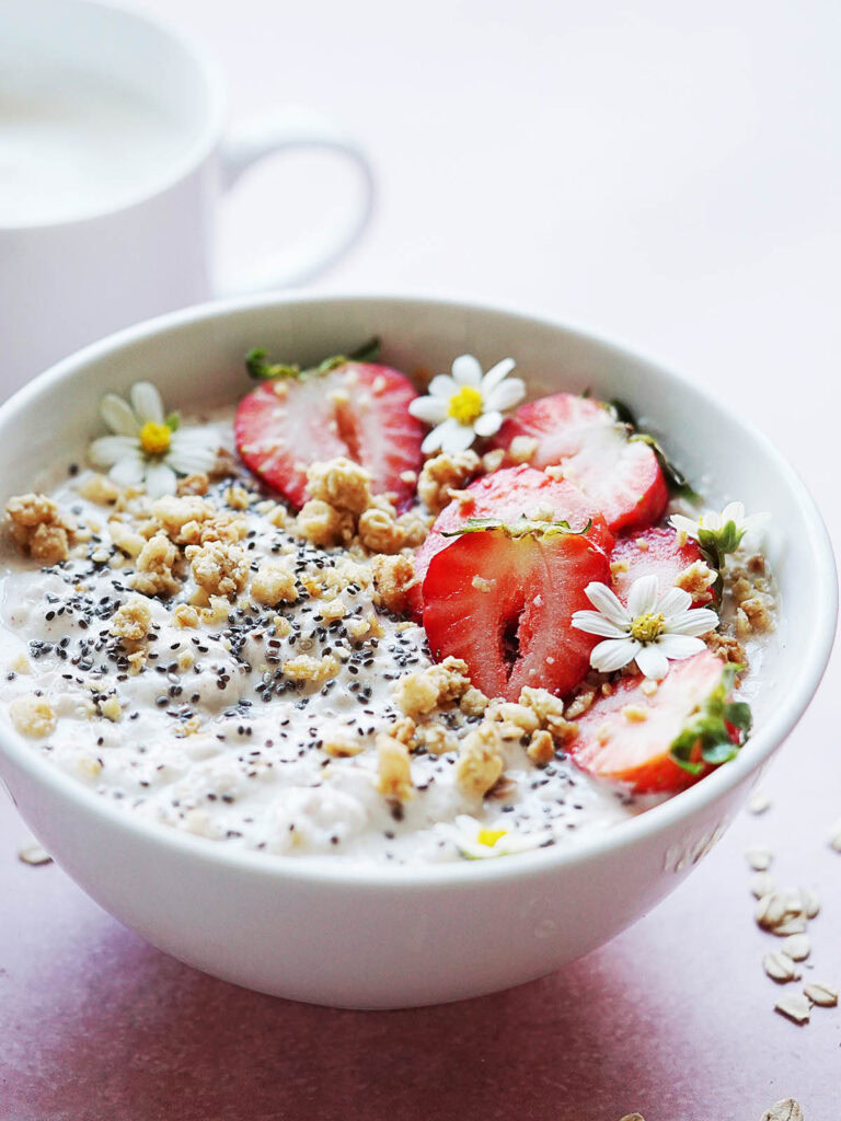 A bowl with yogurt topped with chia seeds, granola and strawberries.