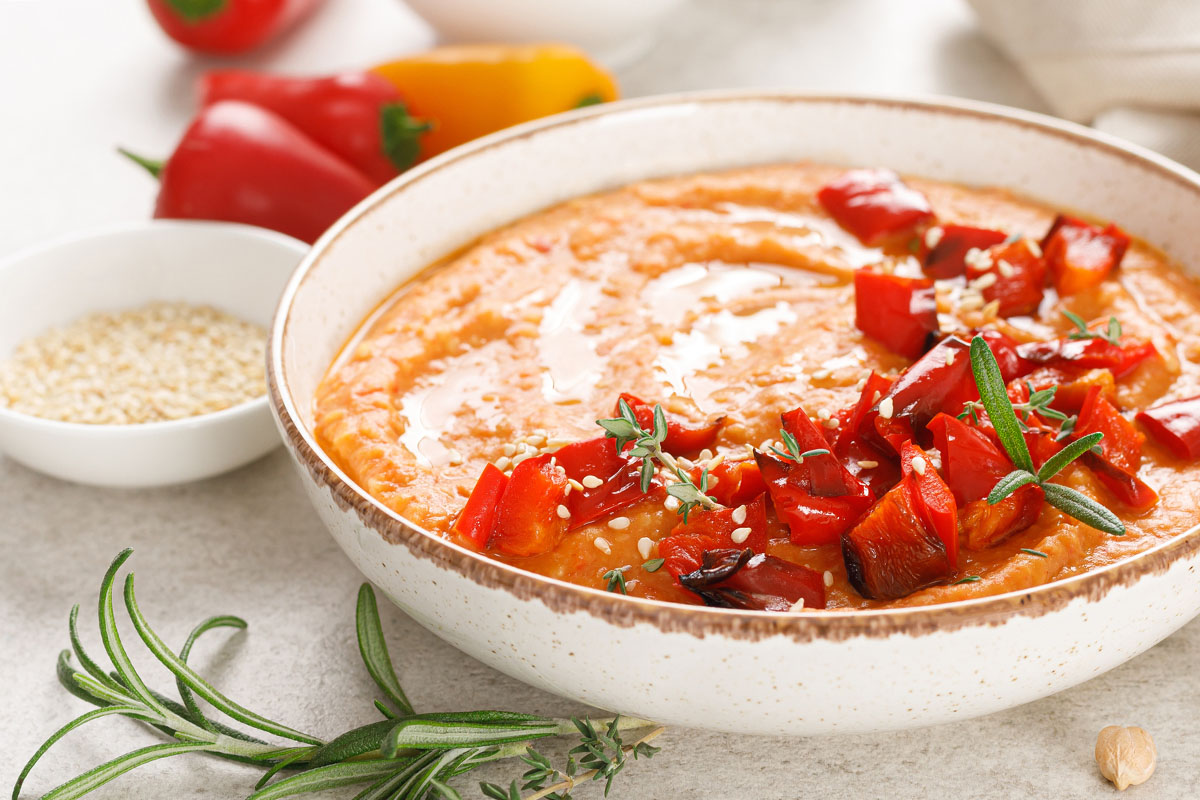 A bowl with roasted red pepper hummus with pita chips.