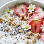 A bowl with yogurt topped with chia seeds, granola and strawberries.