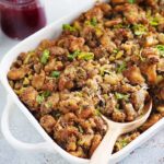 A serving dish with sausage stuffing and a spoon.