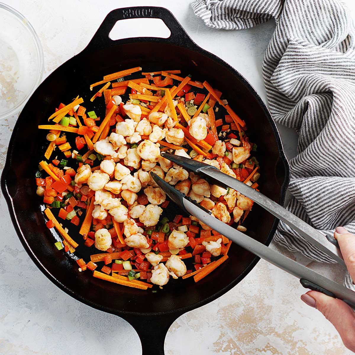 Sauteing shrimp with carrots and onions on a skillet.