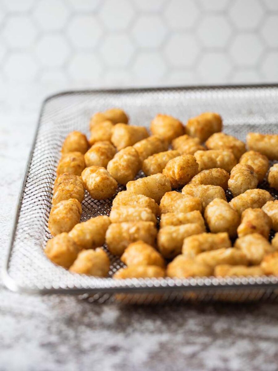 Cooked tater tots on an air fryer tray.