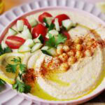 Hummus with cucumber, tomatoes and chickpeas on a pink plate.