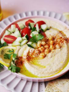 Hummus with cucumber, tomatoes and chickpeas on a pink plate.