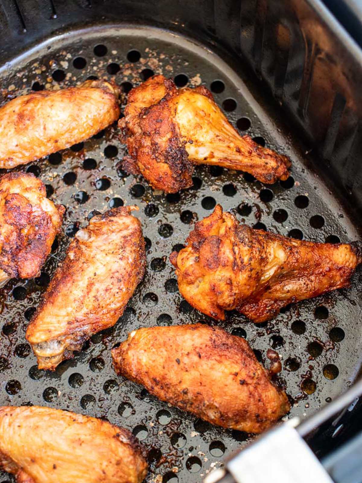Seasoned chicken wings cooking in an air fryer basket.