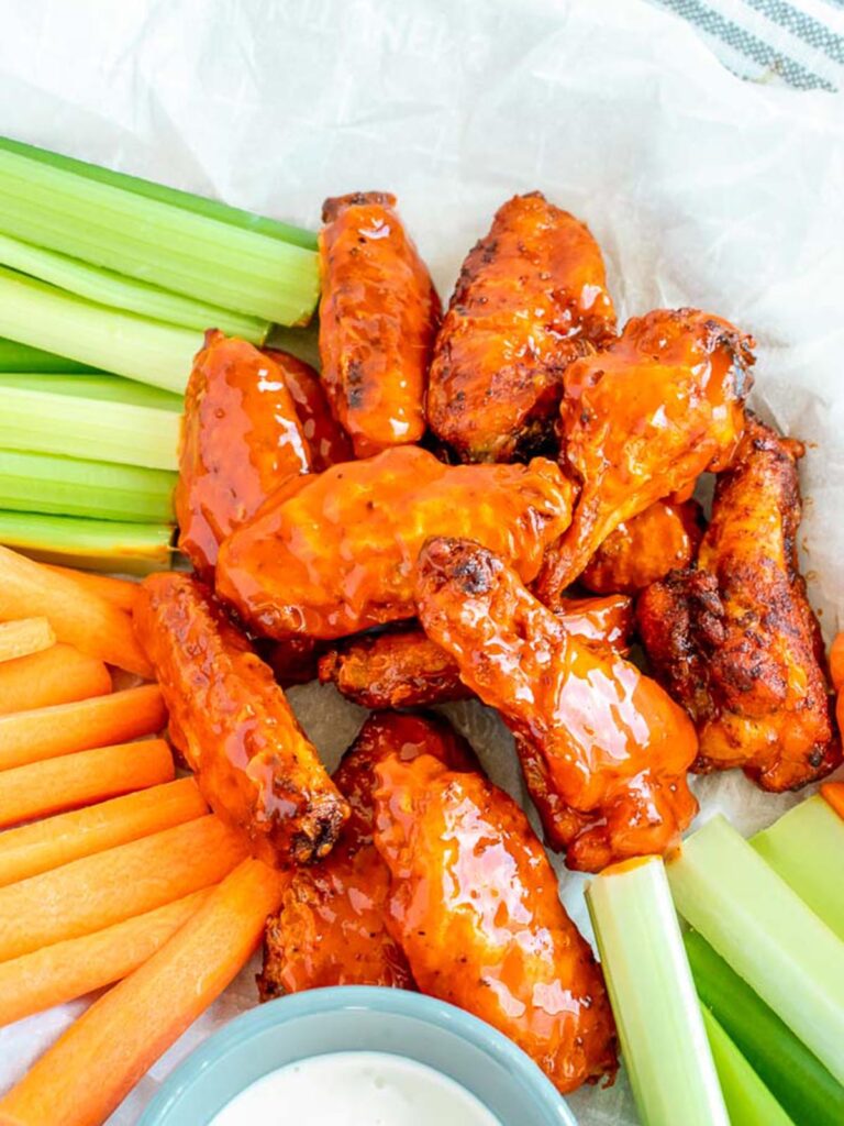 A pile of orange buffalo chicken wings served with carrot sticks, celery stalks, and a small bowl of dipping sauce.