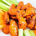 A pile of buffalo chicken wings served with celery and carrot sticks.