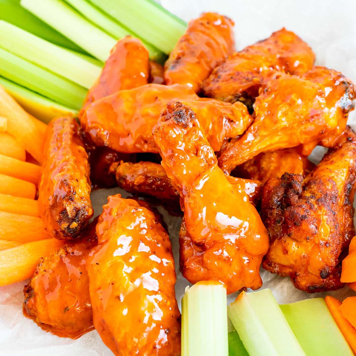 A pile of buffalo chicken wings served with celery and carrot sticks.