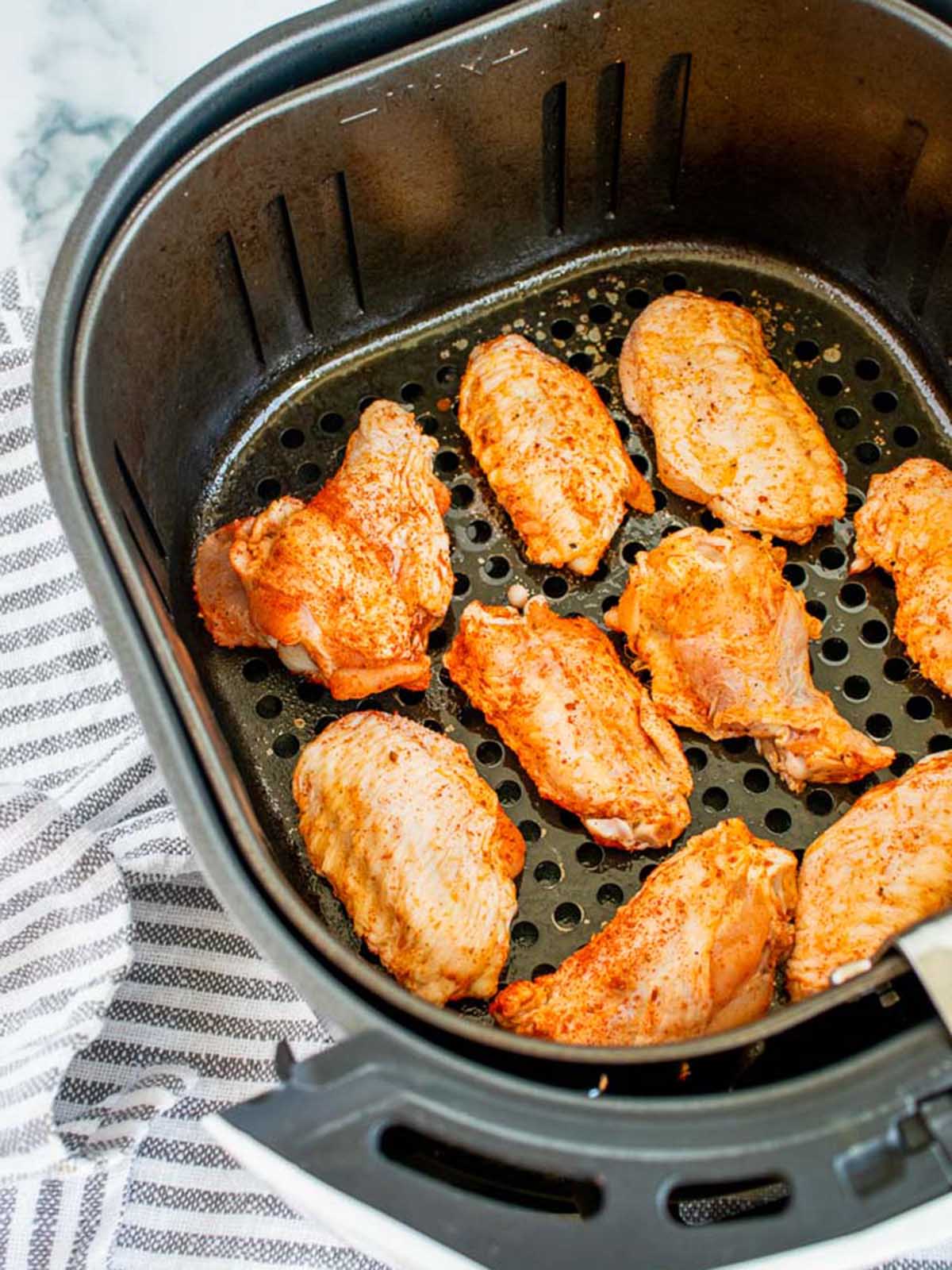 Seasoned raw chicken wings arranged in an air fryer basket.