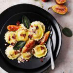 A black plate with cooked Ravioli with Figs, Bacon & Sage.