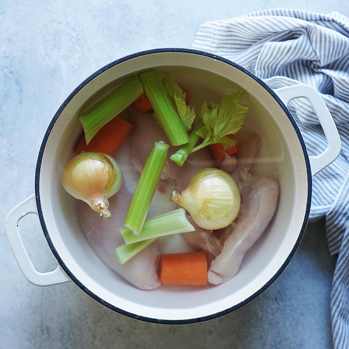 Raw chicken, carrots, celery, and whole onions in a pot of water.
