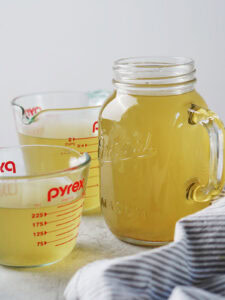 Two glass measuring cups and a mason jar filled with golden-colored broth.