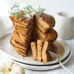 A stack of pancakes with a wedge cut out, a fork lifting a piece, and a white pumpkin nearby.