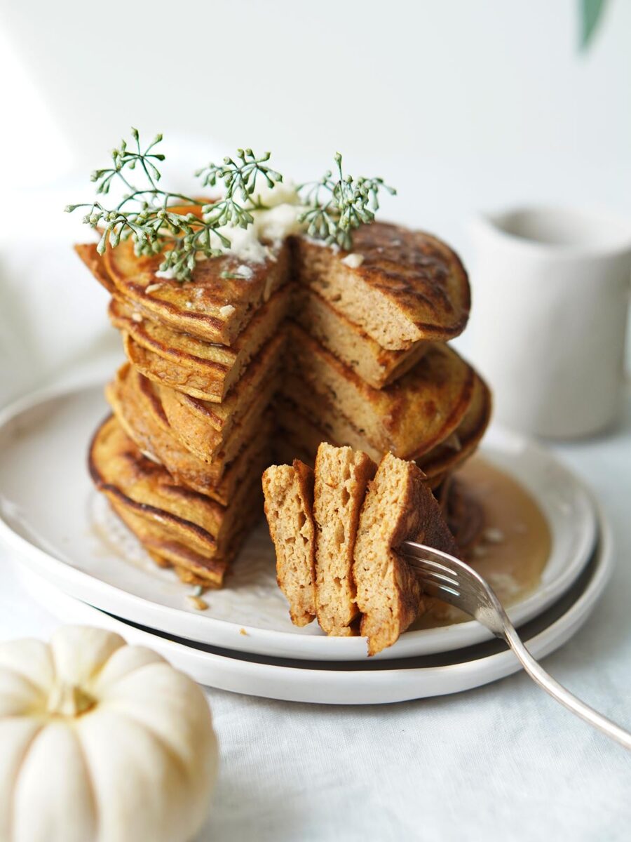A stack of pancakes with a wedge cut out, a fork lifting a piece, and a white pumpkin nearby.